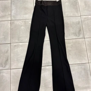 Svarta leggingsbyxor från Zara - Svarta leggingsbyxor från Zara med bred, glansig midjeresår och raka ben som slutar i en lätt bootcut. Byxorna har en stilren look och är gjorda i ett stretchigt material som sitter bekvämt. Perfekta för dig som gillar en enkel men trendig stil.