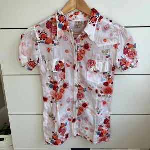 Vit blommig skjorta med kort ärm - Säljer en vit skjorta från Indiska med färgglatt blommigt mönster. Skjortan har bra passform och klassiskt krage. Pris går att diskutera, skriv gärna om du har några frågor! ❤️