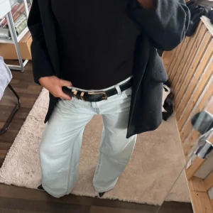 Svart skärp med guldspänne - Snyggt svart bälte i skinn med ett stilrent, fyrkantigt guldspänne. Perfekt accessoar för att lyfta jeans eller byxor och ge outfiten en clean och klassisk touch. Bältet har enkel design och passar till många olika stilar.