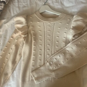Beige stickad tröja med volang från Object - Superfin beige stickad tröja från Object med coola volangdetaljer på axlarna och ett unikt strukturerat mönster framtill. Tröjan har ribbade muddar och rund hals, perfekt för dig som gillar trendiga detaljer och mjuka material. Köpte för 599kr och tröjan är aldrig änvänd då priset är lite högre! men tveka aldrig på att lägga bud!!