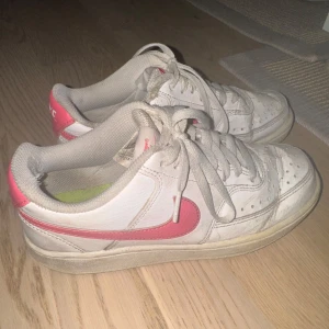 Nike Air Force 1 - Säljer ett par klassiska Nike Air Force 1 sneakers i vitt skinn med rosa swoosh och hälparti. Dom är använda en hel del och har vissa slitningar som ni ser på bilderna.