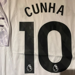 Manchester United Cunha 10 bortatröja M - Säljer en Manchester United bortatröja med Cunha och nummer 10 på ryggen. Tröjan är vit med ljusa mönster, Premier League-logga, Adidas-märke och Snapdragon sponsortryck. Slim fit i lätt och ventilerande polyester, kortärmad modell.