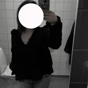 Svart blus med spets och v-ringning - Säljer en svart blus med v-ringning och fina spetsdetaljer längs urringningen. Blusen har långa ärmar med lätt puff och en lös passform som ger en avslappnad men ändå stilren look. Perfekt att matcha med jeans eller kjol. Finns även på Vinted!