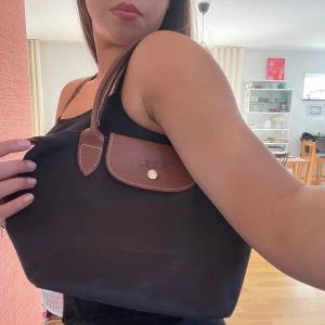 Liten longchamp väska  - Brun liten longchamp, som man kan ha på axeln och i handen. Det är en le pliage modell men storleken på väskan är en äldre årsmodell. Säljer då jag har en annan i en annan färg,