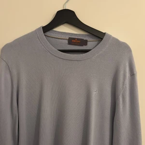 Ljusblå bomullströja från Morris - Säljer en stilren ljusgrå tröja från Morris i 100% pima bomull. Tröjan har rund halsringning, diskret broderad logga på bröstet och ribbade muddar. Perfekt för dig som gillar klassisk och clean stil.