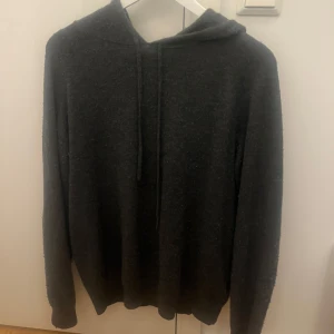 Mörkgrå hoodie från Tiger of Sweden - Mysig mörkgrå hoodie från Tiger of Sweden med huva och dragsko. Tröjan är stickad och har långa ärmar, perfekt för kyliga dagar. Enkel och stilren design som passar till det mesta.