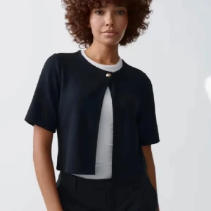 Mörkblå kortärmad kofta med knapp - Stilren mörkblå kofta med korta ärmar och en snygg guldig knapp framtill. Modellen är croppad och har en öppen front, perfekt att slänga över en t-shirt eller linne. Enkel och clean design som passar till många outfits.