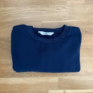 Mörkblå sweatshirt från H&M - En stilren mörkblå sweatshirt från H&M med rund halsringning och ribbade muddar vid ärmslut och nederkant. Tröjan är storlek 158-164 och har en hyfsat slim passform. Perfekt för lite kyligare dagar. Om ni har några funderingar så bara skriv!