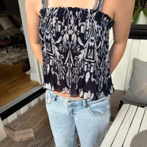 Mönstrad mörkblåvit linnetopp - Säljer en luftig linnetopp med smala axelband. Toppen är marinblå med vitt mönster och har en lätt rynkad kant upptill och nertill. Perfekt för varma dagar och enkel att styla med jeans eller kjol.💕