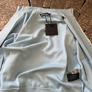 Ljusblå track jacket från Palm Angels - Palm Angels ljusblå kofta med vita ränder. Vi kan även diskutera priset!