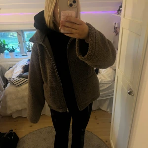 Brun teddyjacka från 157, storlek M - Mysig brun teddyjacka från 157 i storlek M. Jackan har en oversized passform, dragkedja framtill och stora fickor. Perfekt för kyliga dagar med sitt fluffiga och varma material. Enkel att matcha med både jeans och mjukisbyxor.