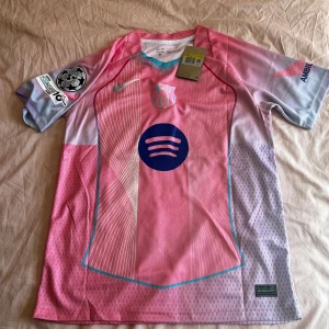 FC Barcelona Tröja - Säljer en FC Barcelona matchtröja. Hög kvalité och snygg design – perfekt för dig som vill ha Barca-looken utan att lägga för mycket pengar. Skön passform Lamine Yamal #10 på ryggen Exklusiv design i rosa/lila nyanser med Spotify-logga Funkar lika bra på träning som till vardags för alla som älskar Barcelona-stilen. 📩 Hör av dig vid frågor! Snabb leverans.