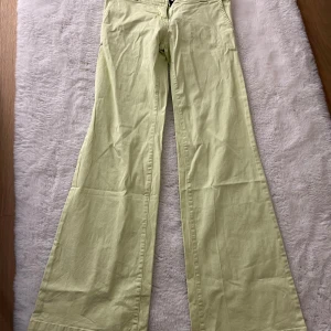 Ljusgula wide low waist byxor med fickor - Snygga ljusgula byxor low waist med breda ben och bakfickor med knappar. Byxorna har en klassisk passform med normal midja och är tillverkade i ett mjukt bomullstyg. Perfekta för dig som vill sticka ut med en fräsch färg och skön stil.