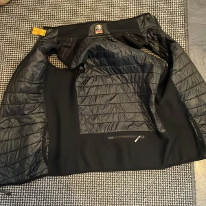Svart Parajumpers jacka Warm Up YL - Säljer en svart Parajumpers Warm Up jacka i storlek YL. Jackan har quiltade partier på insidan, orange detaljer och klassisk PJS-logga. Materialet är polyester och jackan har dragkedja. Perfekt för dig som vill ha en stilren och funktionell jacka.