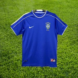 Brasilien - VM 1998 - Nyskick/helt oanvänd Brasilien bortatröja från VM 1998. En vacker och ikonisk design där stjärnor som R9 bar denna tröja. Tveka inte att höra av dig för mer bilder och frågor!