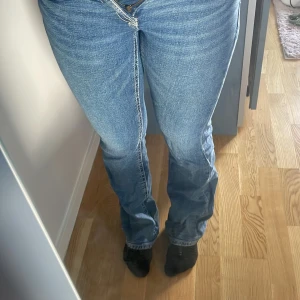 Blå bootcut jeans med normal passform - Säljer ett par klassiska blå jeans med bootcut-modell och normal passform. Jeansen har fem fickor, dragkedja och knapp framtill samt snygga sömmdetaljer. Perfekta för dig som gillar en tidlös look med lite utsvängda ben.