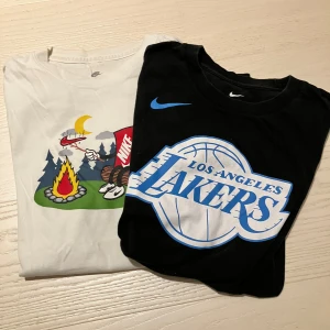 Nike t-shirts, vit med tryck & svart Lakers - Två Nike t-shirts i storlek L. En vit med färgglatt tryck av lägereld och Nike-logga, och en svart med stor Los Angeles Lakers-logga i blått och vitt. Båda har klassisk passform och rund hals. Perfekta för dig som gillar sportig och avslappnad stil. 147-158cm 