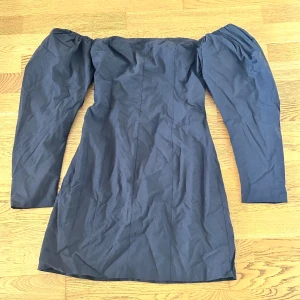 Svart offshoulder klänning H&M - Snygg svart kortklänning från H&M med offshoulder och långa puffärmar. Klänningen har smockad rygg för extra komfort och stängs med hyskor.  Helt ny och perfekt för dig som gillar stilrena och trendiga plagg.