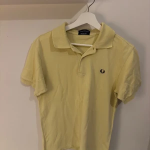 Gul pikétröja från Fred Perry - Snygg gul pikétröja från Fred Perry med klassisk krage och korta ärmar. Tröjan har den ikoniska Fred Perry-loggan broderad på bröstet och är tillverkad i mjuk bomull. Perfekt för en fräsch och sportig look.