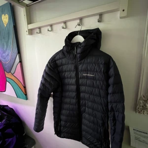 Svart dunjacka från Peak Performance - Säljer en svart dunjacka från Peak Performance med huva och dragkedja, perfekt nu inför vintern! Jackan är quiltad med horisontella sömmar och har en clean, sportig look. Perfekt för kalla dagar och riktigt skön att bära. Snygg passform och diskret logga på bröstet. Pris kan diskuteras!