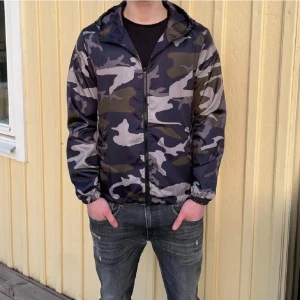 Camouflage vindjacka med huva - Säljer en snygg vindjacka med camouflagemönster i mörka och ljusa toner. Jackan har huva, dragkedja framtill och resår vid ärmslut. Perfekt för dig som vill ha en streetig look och gillar att sticka ut.