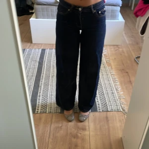 Ginatricot wide blå jeans, storlek 32 - Säljer ett par mörkblå jeans från Ginatricot i storlek 32. Modellen är midwaist och breda, raka ben för en chill och trendig look. Klassisk femficksdesign med kontrastsömmar och knappstängning framtill. Perfekt för dig som gillar loose fit och stilrena jeans.