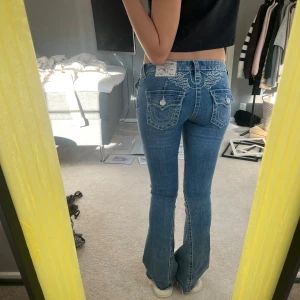 True Religion blå bootcut jeans - Säljer ett par blå jeans från True Religion med bootcut passform och låg midja. Jeansen har vita broderade vingar strax över rumpan ! Säljer då dom inte kommer till användning längre💕 storlek 24 och dom är avklippta där nere men passar bra på mig som är 165💕 kom gärna med prisförslag!