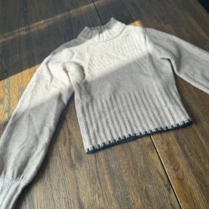 Beige stickad polotröja från Bubbleroom - Supermysig beige stickad polotröja från Bubbleroom i storlek XS. Tröjan har ribbade detaljer vid hals, ärmslut och nederkant samt en diskret mörk kant längst ner. Perfekt för lager-på-lager och chill höst- och vinterstil.