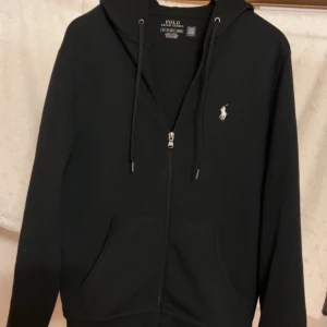 Svart hoodie från Polo Ralph Lauren - Svart hoodie från Polo Ralph Lauren med dragkedja, huva med snörning. Äkta såklart använd 1-2 veckor då den är för stor. Hör av er om ni vill förhandla!