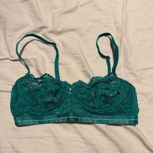 Grön spets bralette från Lounge - Snygg grön bralette från Lounge med spetsdetaljer och justerbara axelband. Modellen har elastiskt band med Lounge-logga och vacker blommig spets över kuporna. Perfekt för dig som gillar en feminin och trendig look.