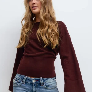 Vinröd tröja med vida ärmar - Vinröd stickad tröja från Gina Young med bred ribbad midja och vida långa ärmar. Tröjan har en tightare passform i midjan och är tillverkad i mjukt material. Perfekt för dig som gillar en stilren look med en twist.