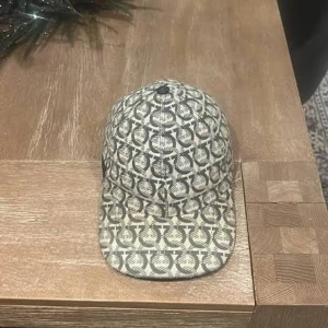 Salvatore Ferragamo mönstrad keps - Snygg keps från Salvatore Ferragamo med beige och svart färg och ett unikt, grafiskt mönster över hela kepsen. Justerbar rem baktill och klassisk böjd skärm. Perfekt accessoar för att lyfta din outfit.