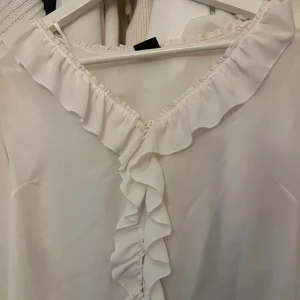 blus - vit blus med knappar och volanger fram till, skriv vid fler bilder eller frågor 