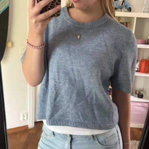 Blå stickad tröja från H&M Divided - Superfin ljusblå stickad tröja från H&M Divided med kort ärm och ribbade kanter. Tröjan har en loose passform och är perfekt till jeans eller kjol. Mjuk och skön, passar både till vår och sommar.