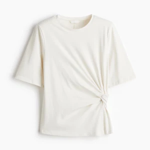 Vit knyt topp med kort ärm - Säljer en stilren vit topp med korta ärmar och rund hals. Toppen har en snygg knyt-detalj på sidan som ger en cool twist till den klassiska looken. Perfekt för dig som gillar enkel men trendig stil. oanvänd med lappen kvar!! 🥰