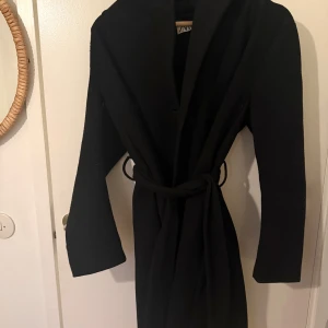 Svart kappa med huva från Zara - Svart kappa från Zara med huva och knytskärp i midjan. Är 164cm och den går ner till knäna för referens! 😊