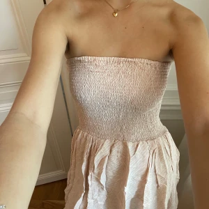 Ljusrosa axelbandslös kortklänning - Supersöt ljusrosa kortklänning med smockad överdel och axelbandslös design. 