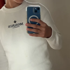 Vit tröja från Morris - Säljer en stilren vit tröja från Morris med broderad logga på bröstet. Tröjan har långa ärmar och ribbade muddar vid ärmslut och nederkant. Perfekt för en avslappnad look. Priset kan diskuteras