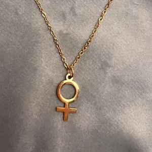 Feminist halsband guld imitation kvinnosymbolen - 10% av det här köpet ger jag till kvinnojouren Karlskrona.   Fint halsband med kvinnosymbolen. Kedjan är justerbar 40-45 cm och berlocken är ca 1 x 1,8 centimeter. Guldimitation. 