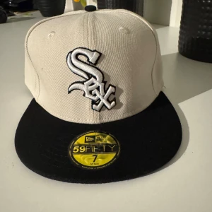 White Sox keps New Era 59FIFTY - Snygg White Sox keps från New Era 59FIFTY med broderad logga fram och text bak. Kepsen är beige med svart skärm och har en klassisk, rak form. Perfekt för dig som gillar baseball eller vill ha en stilren streetwear-accessoar.