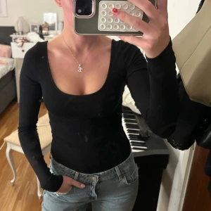 Svart långärmad body från Gina Tricot - En svart långärmad body från Gina Tricot med djup rundad urringning. Modellen är tight och sitter snyggt mot kroppen. Perfekt att styla med jeans eller kjol för en clean look. Gjord i mjuk bomullsmix som känns skön hela dagen.