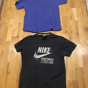 Svart Nike Sportswear t-shirt L - Svart t-shirt från Nike med stort vitt Nike Sportswear-tryck på bröstet och färgade detaljer under loggan. Klassisk rund halsringning med grön insida. Skön passform och perfekt för en sportig look.