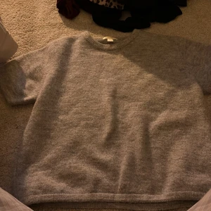 Grå stickad tröja från Gina Tricot - Mysig grå stickad tröja från Gina Tricot i storlek 170. Tröjan har rund halsringning, korta ärmar och är tillverkad i ett mjukt material som passar perfekt för kyligare dagar. Enkel och stilren design som är lätt att matcha.