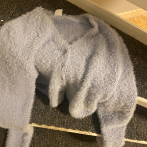 Ljuslila fluffig kofta från Lindex - Supermjuk och fluffig ljuslblp kofta från Lindex med v-ringning och knappar framtill. Perfekt för dig som vill ha en cozy och trendig look. Koftan har lång ärm och är riktigt gosig att bära under kyliga dagar.