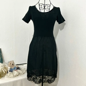 Kortarmad svart nattlinne med spetsdetaljer - Svart nattlinne med v-ringad hals och spetsdetaljer samt liten rosett framtill. Den nedre delen är lite genomskinlig. Passar storlek 32-34. Dockan har storlek 34.