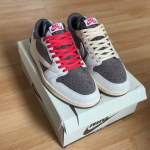 Nike Air Jordan 1 Low Travis Scott - Nike Air Jordan 1 Low Travis Scott med coola kontrasterande snören, ett par röda och ett par beige. Skorna har grå mocka på tå och paneler, vit skinn på sidorna och bak, samt mörkbruna detaljer. Ikoniska Air Jordan-loggan och Travis Scott-emblem broderade i rött på hälen. Priset kan diskuteras👍