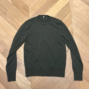 Mörkgrön långärmad tröja från Uniqlo (PRIS KAN DISKUTERAS!) - En stilren mörkgrön tröja från Uniqlo med rund hals och lång ärm. Tröjan är tunn och har en normal passform, perfekt att bära över en t-shirt. Materialet är mjukt och känns skönt mot huden, och den har ribbade muddar vid ärmslut och nederkant.
