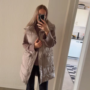 Beige lång väst från Lager 157 - Lång,  beige väst  från Lager 157 med stora fickor framtill. Västen har dragkedja och tryckknappar hela vägen ner. Perfekt för lager-på-lager och en chill streetstyle-look.