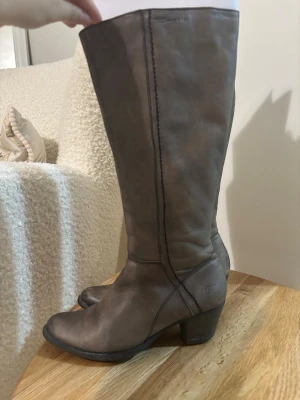 Bruna stövlar med klack från Tamaris - Snygga bruna stövlar från Tamaris i skinn med markerade sömmar och rund tå. Stövlarna har en låg klack och dragkedja på insidan för enkel på- och avtagning. Perfekt till höst- och vinterlooken, stilrena och lätta att matcha.