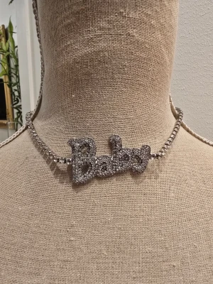 Strass halsband  - Bilden visar ett halsband med texten 'Baby' i glittriga stenar, men ingen väst finns med.